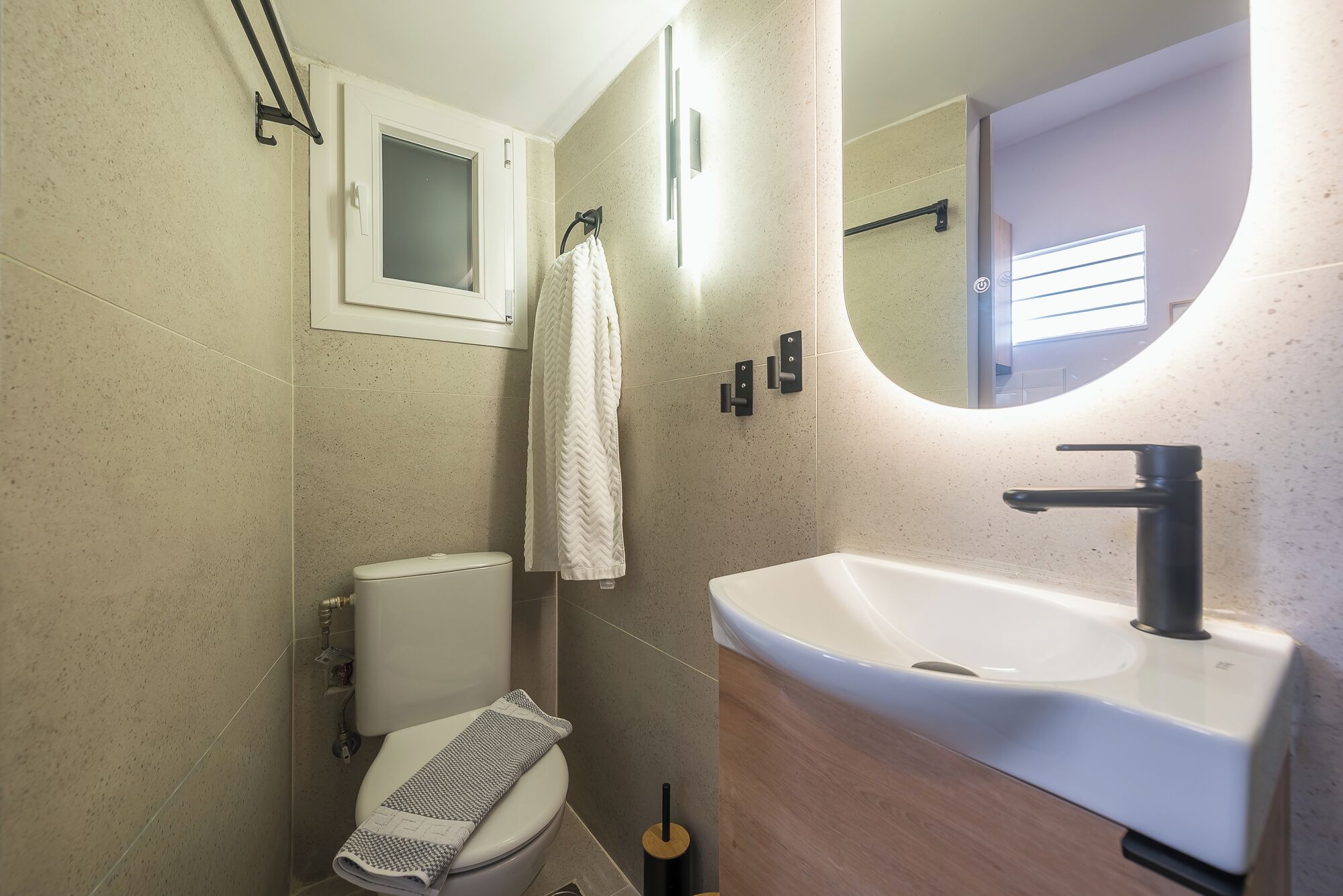 A bathroom with a toilet, sink, mirror, and towel rack.