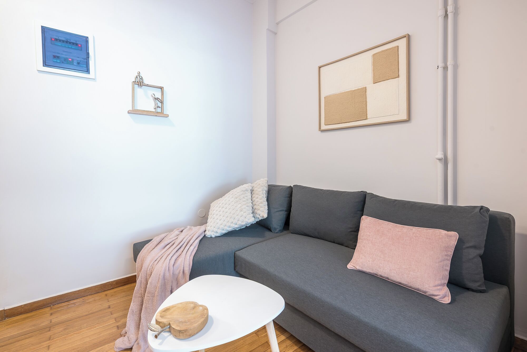 A modern living room with a grey sofa, a white coffee table, and a small white side table. There are two framed artworks on the wall and a blue sign above the sofa.