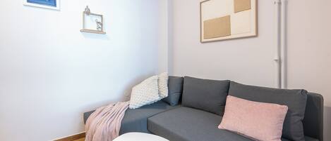 A modern living room with a grey sofa, a white coffee table, and a small white side table. There are two framed artworks on the wall and a blue sign above the sofa.
