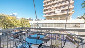 A balcony with a table and chairs, overlooking a street with parked cars and a building with balconies. - Prime City Stay by Cloudkeys (Athens)