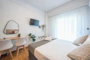 A hotel room with a bed, a desk with a chair, a TV mounted on the wall, and a window with curtains. - Prime City Stay by Cloudkeys (Athens)