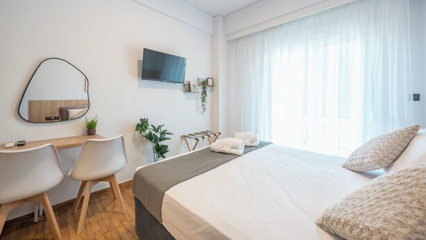 A hotel room with a bed, a desk with a chair, a TV mounted on the wall, and a window with curtains. - Prime City Stay by Cloudkeys (Athens)