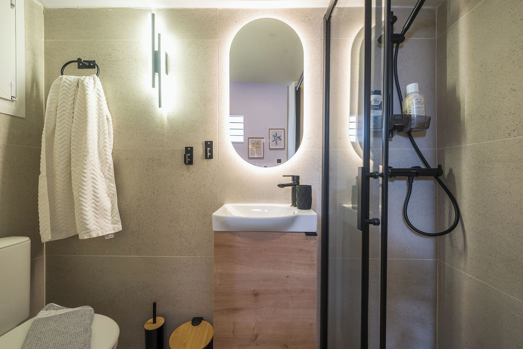 A modern bathroom with a glass shower enclosure, a white sink, and a towel rack.