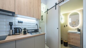 A modern kitchen with a coffee maker, kettle, and toaster, a wooden cabinet, and a sliding door leading to a bathroom with a sink and mirror. - Prime City Stay by Cloudkeys (Athens)