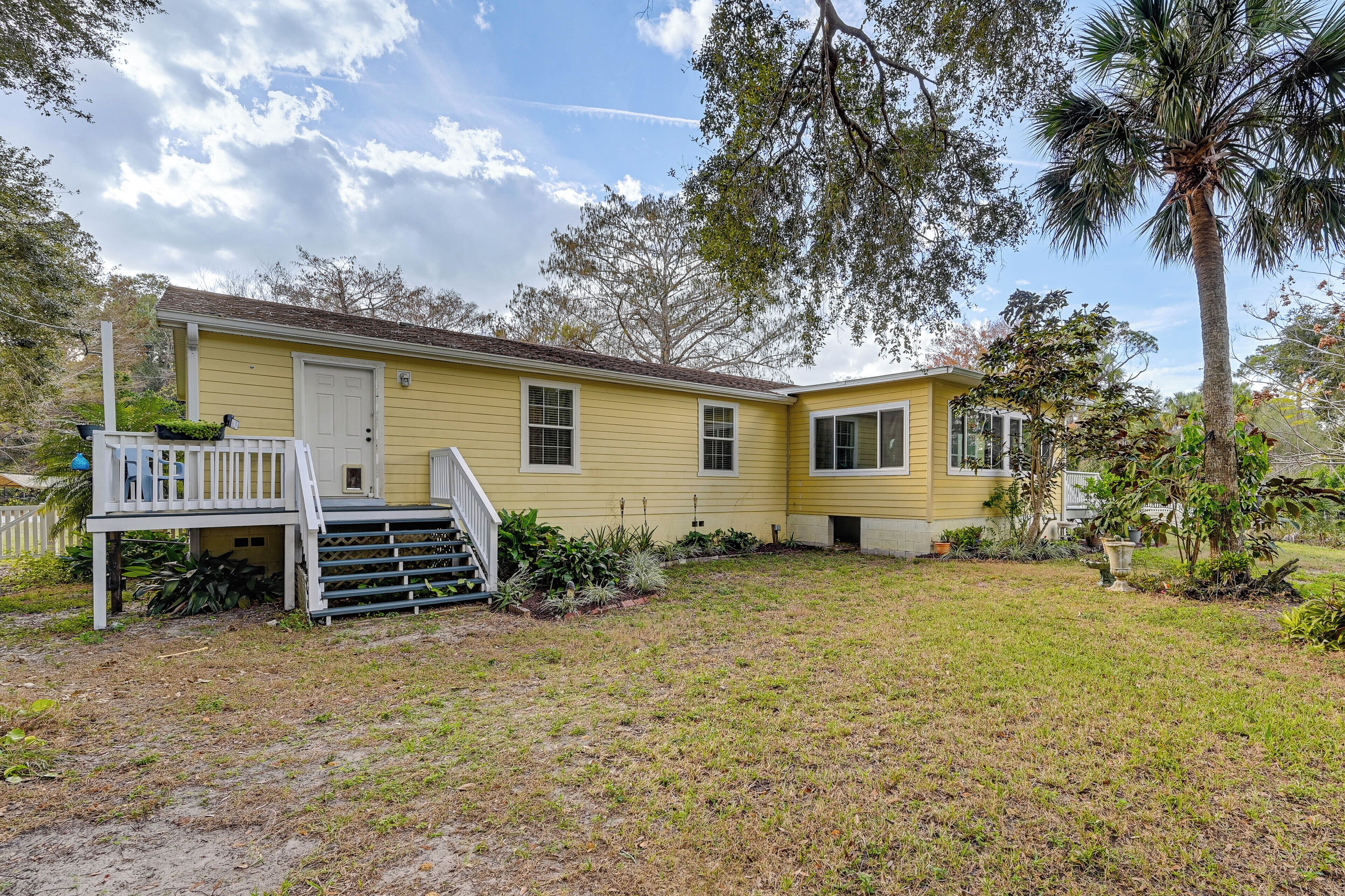 A yellow single-story house with a front porch, a small front yard, and a palm tree.