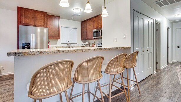 A modern kitchen with wooden cabinets, stainless steel appliances, and a marble countertop. There are three wicker bar stools and pendant lights above the counter. - Relax Fireside: Family Home 6 Mi to Dtwn Beaufort! (Beaufort)
