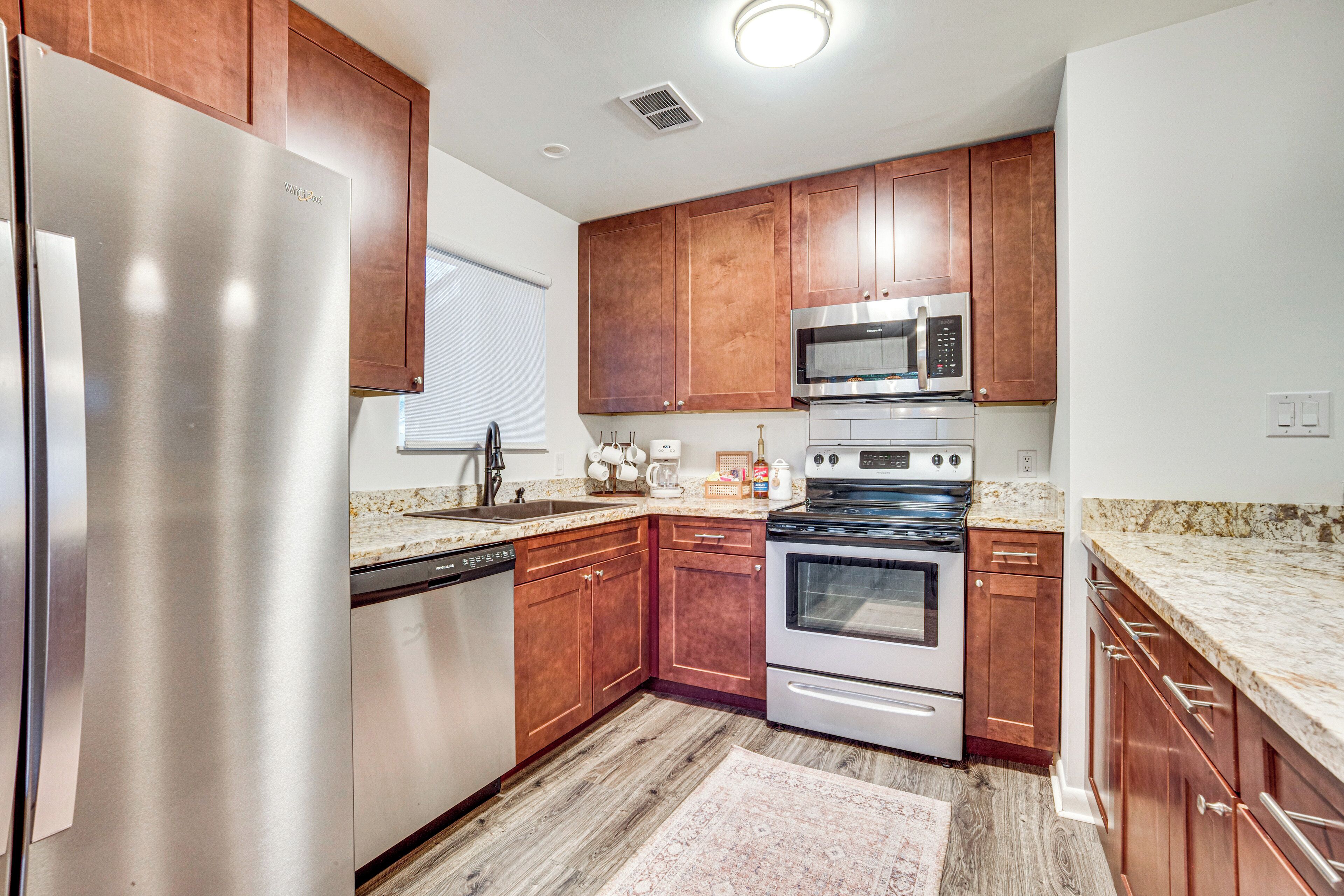A modern kitchen with stainless steel appliances, wooden cabinets, granite countertops, and a patterned rug.