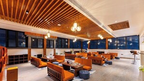 Ein geräumiger Lounge-Bereich mit Holzbodenpaneelen, großen Fenstern und orangefarbenen Sitzmöglichkeiten.