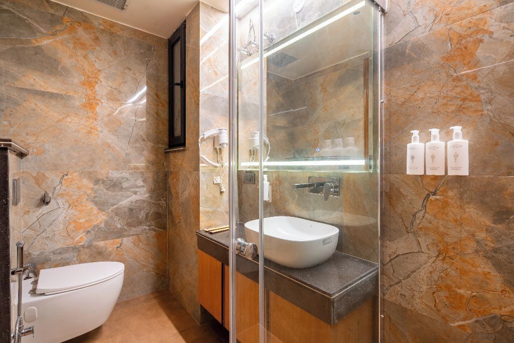 A bathroom with a marble wall, a glass-enclosed shower, a white sink, and toiletries on the wall.