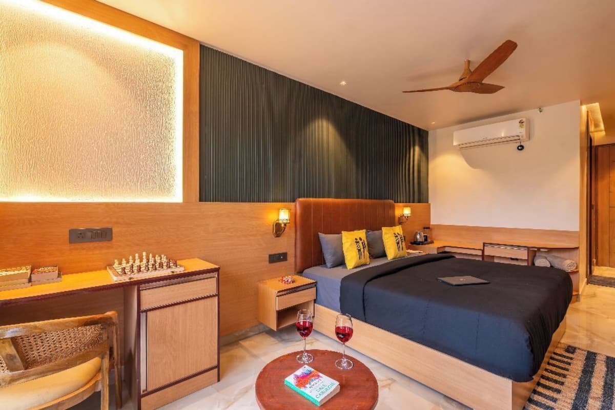 A hotel room with a wooden desk, a bed with a dark blue bedspread, a ceiling fan, and an air conditioning unit.