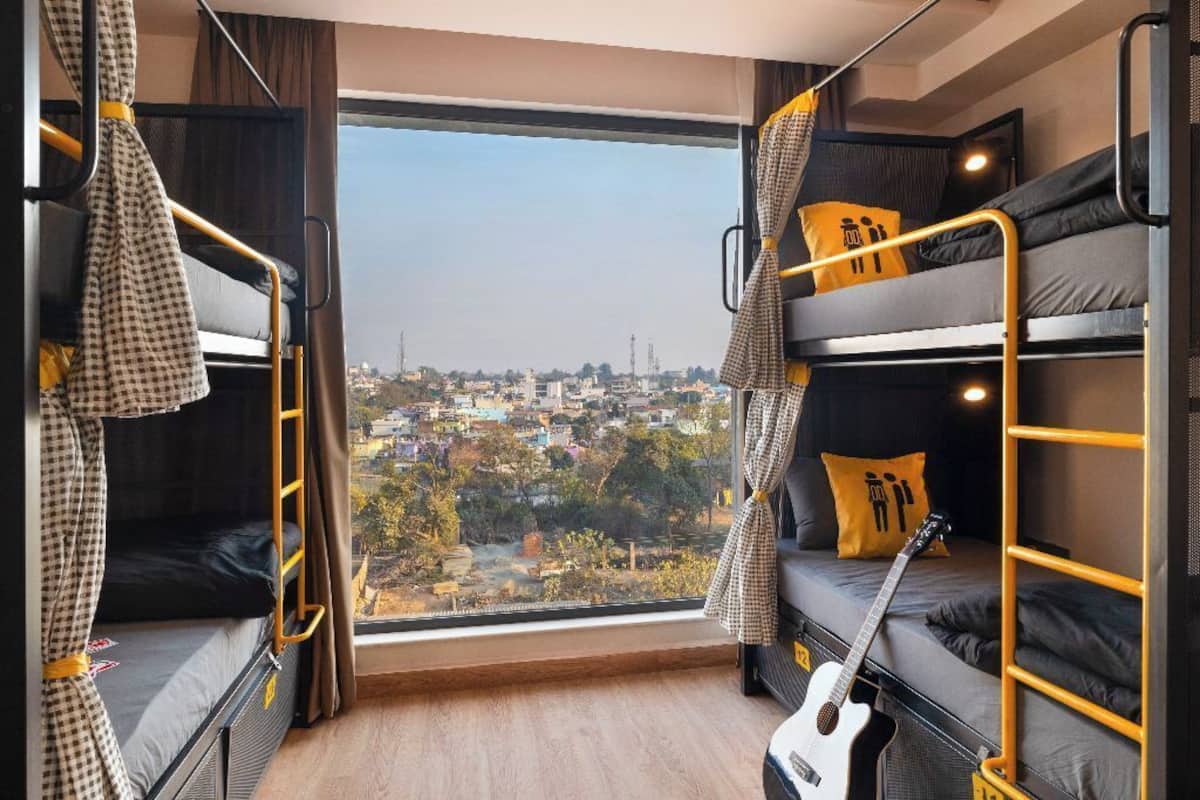 A dormitory room with bunk beds, a guitar, and a city view through a large window.
