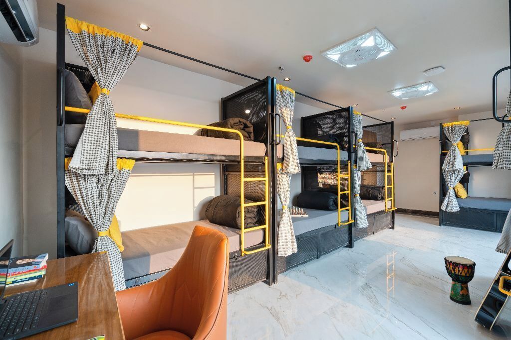 A dormitory room with bunk beds, a desk with a laptop, and a drum.