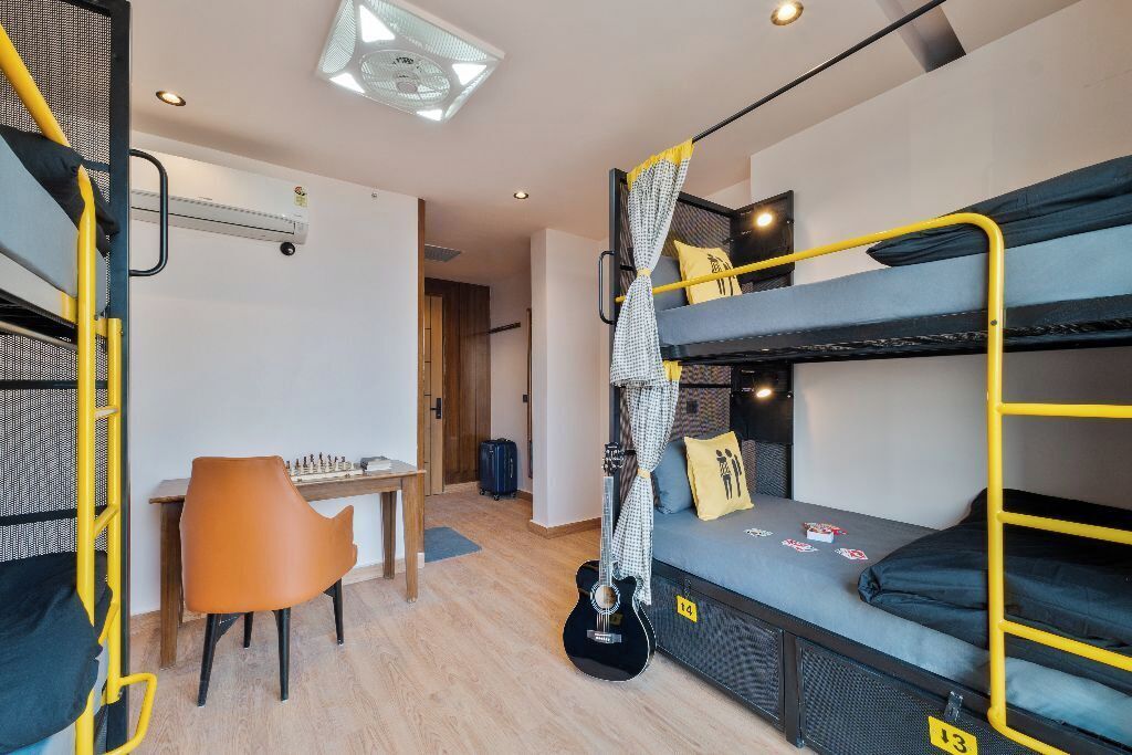 Ein Studentenwohnheimzimmer mit Etagenbetten, einem Schreibtisch, einem Stuhl und einer Gitarre.