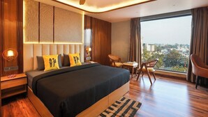 Ein modernes Hotelzimmer mit einem großen Bett, einem Deckenventilator, Blick auf die Stadt und einem kleinen Tisch mit Stühlen.