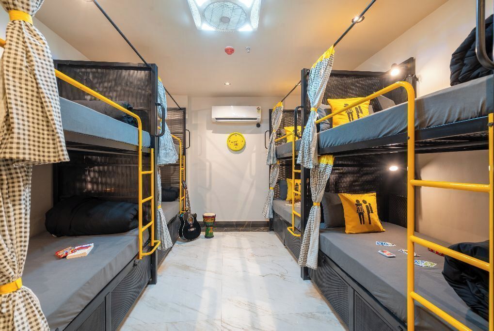 A dormitory room with bunk beds, a fan, a clock, and a small drum.