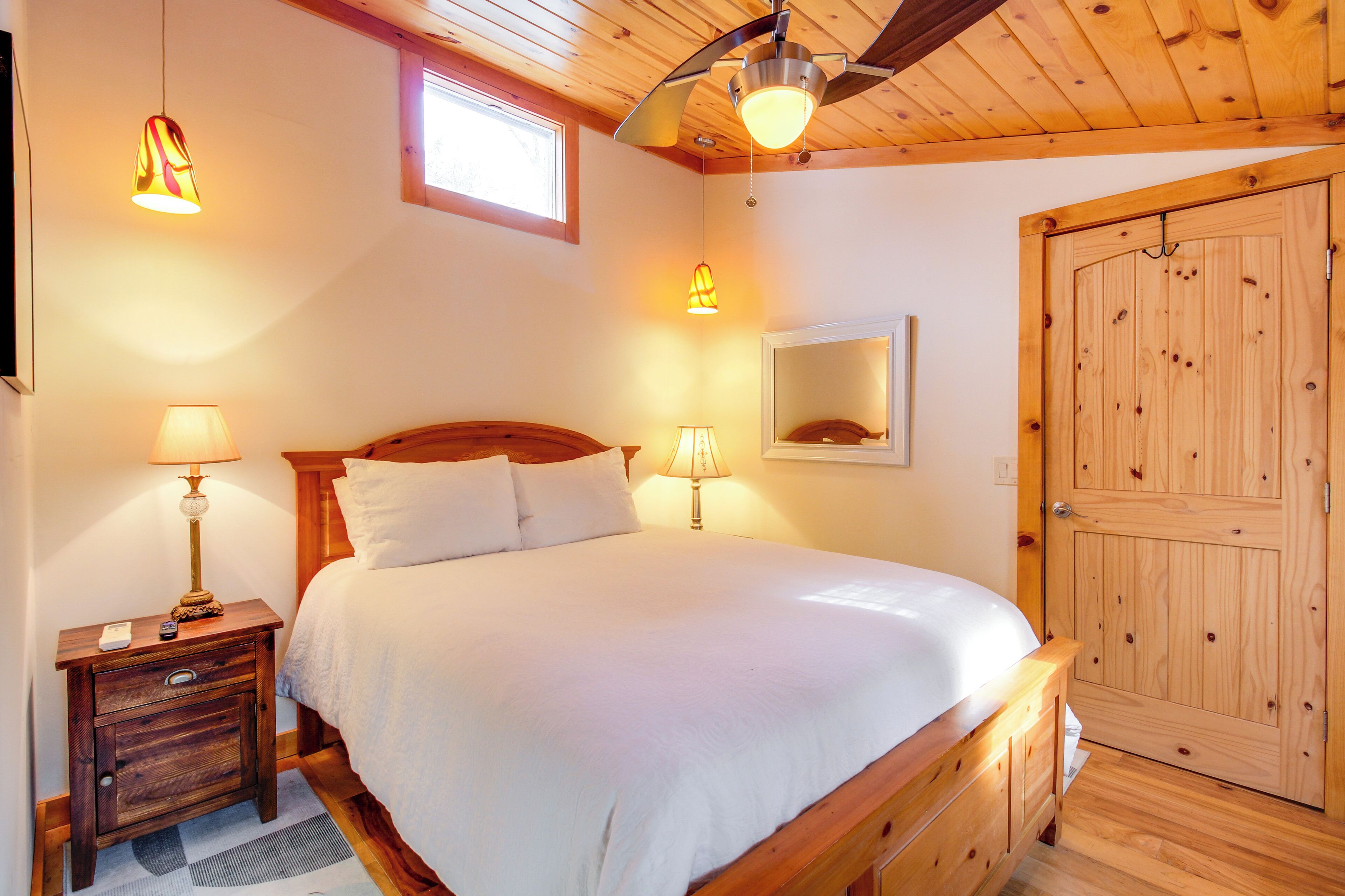 Ein Schlafzimmer mit einem hölzernen Bett, zwei Nachttischlampen, einem Nachttisch, einem Deckenventilator, einer Holztür und einem Fenster.