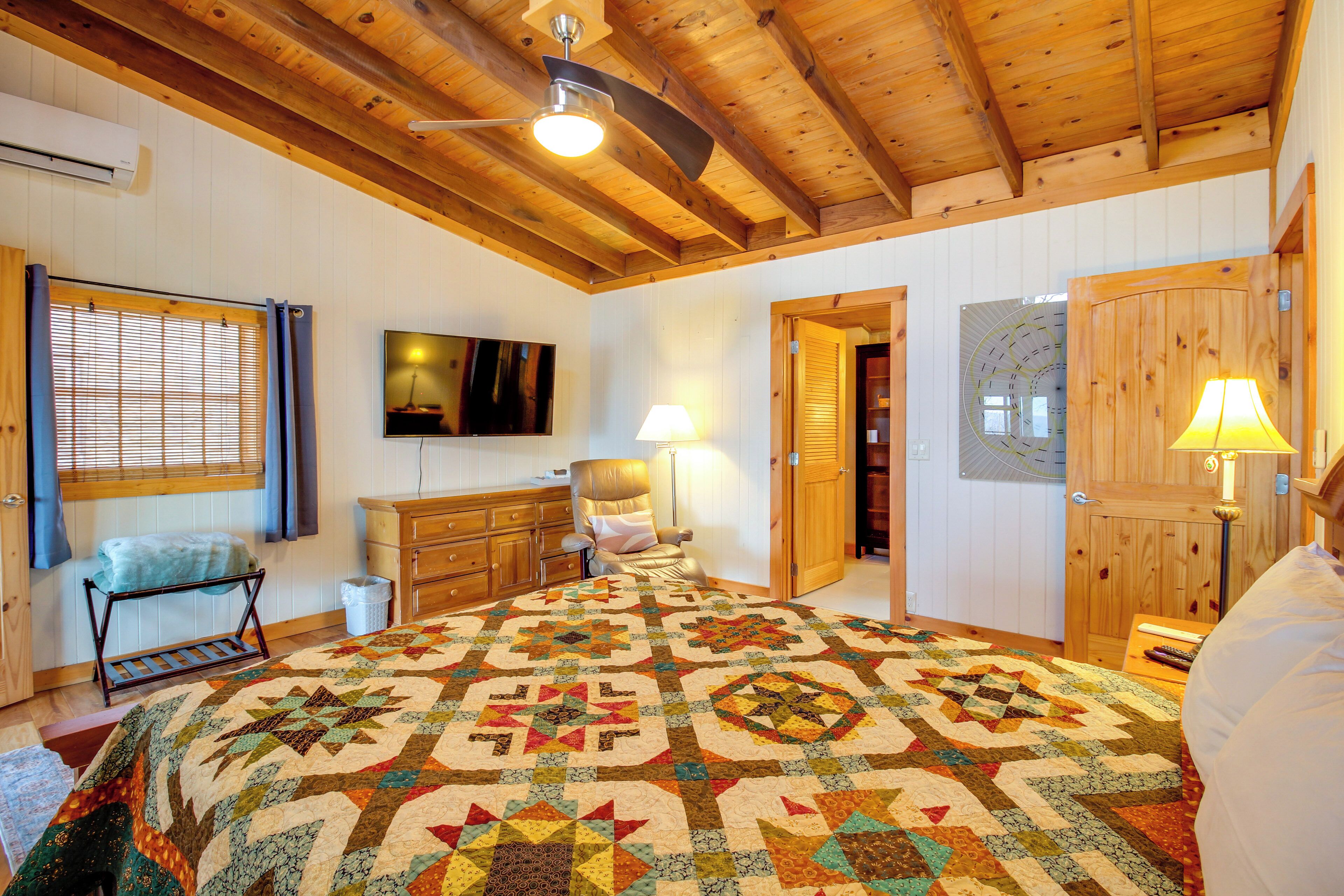 Ein gemütliches Schlafzimmer mit einem großen Bett, Holzbalken an der Decke, einem Fernseher, einem Schreibtisch und einem Stuhl.