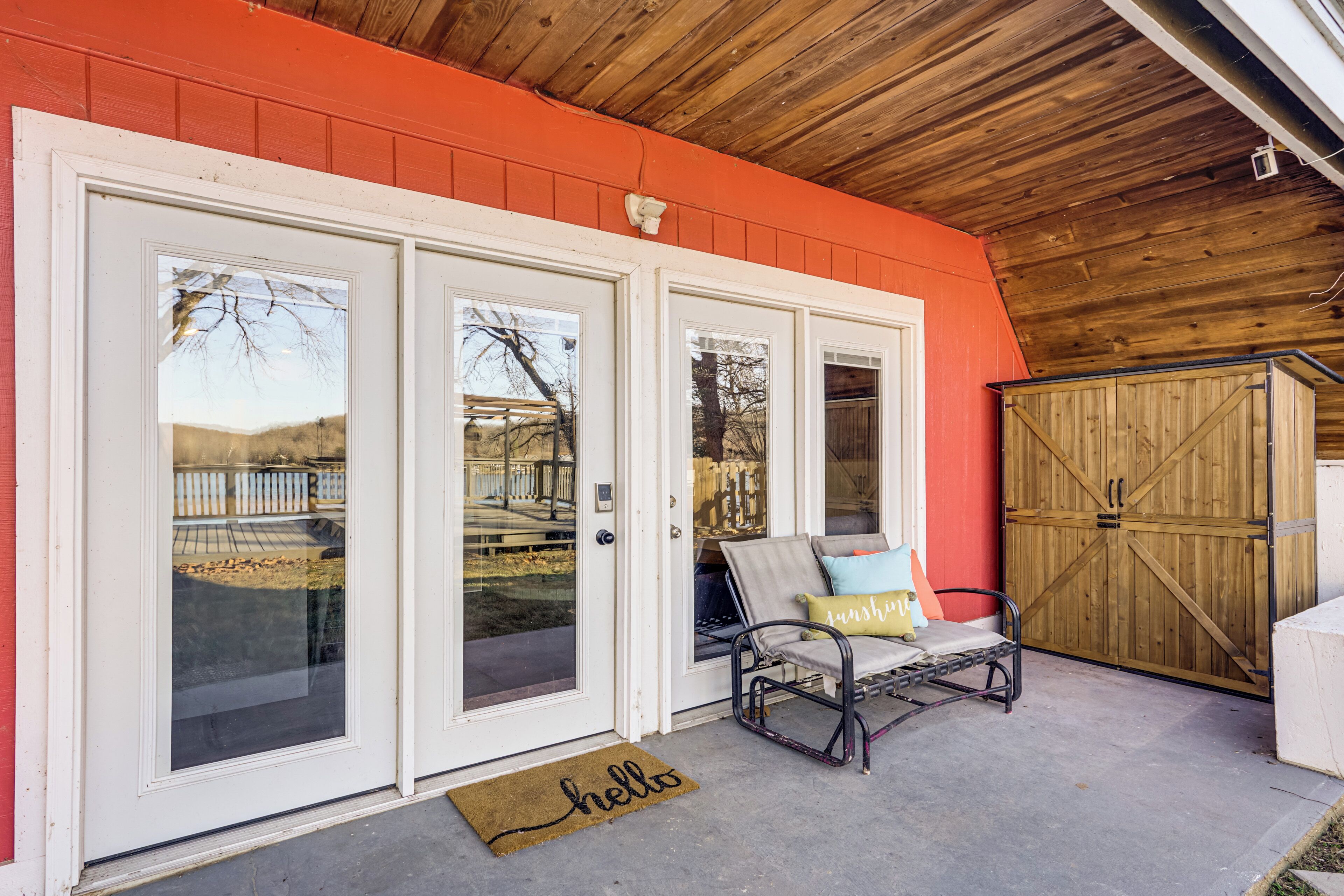 A covered patio with a wooden ceiling, a red wall, and a sliding glass door.