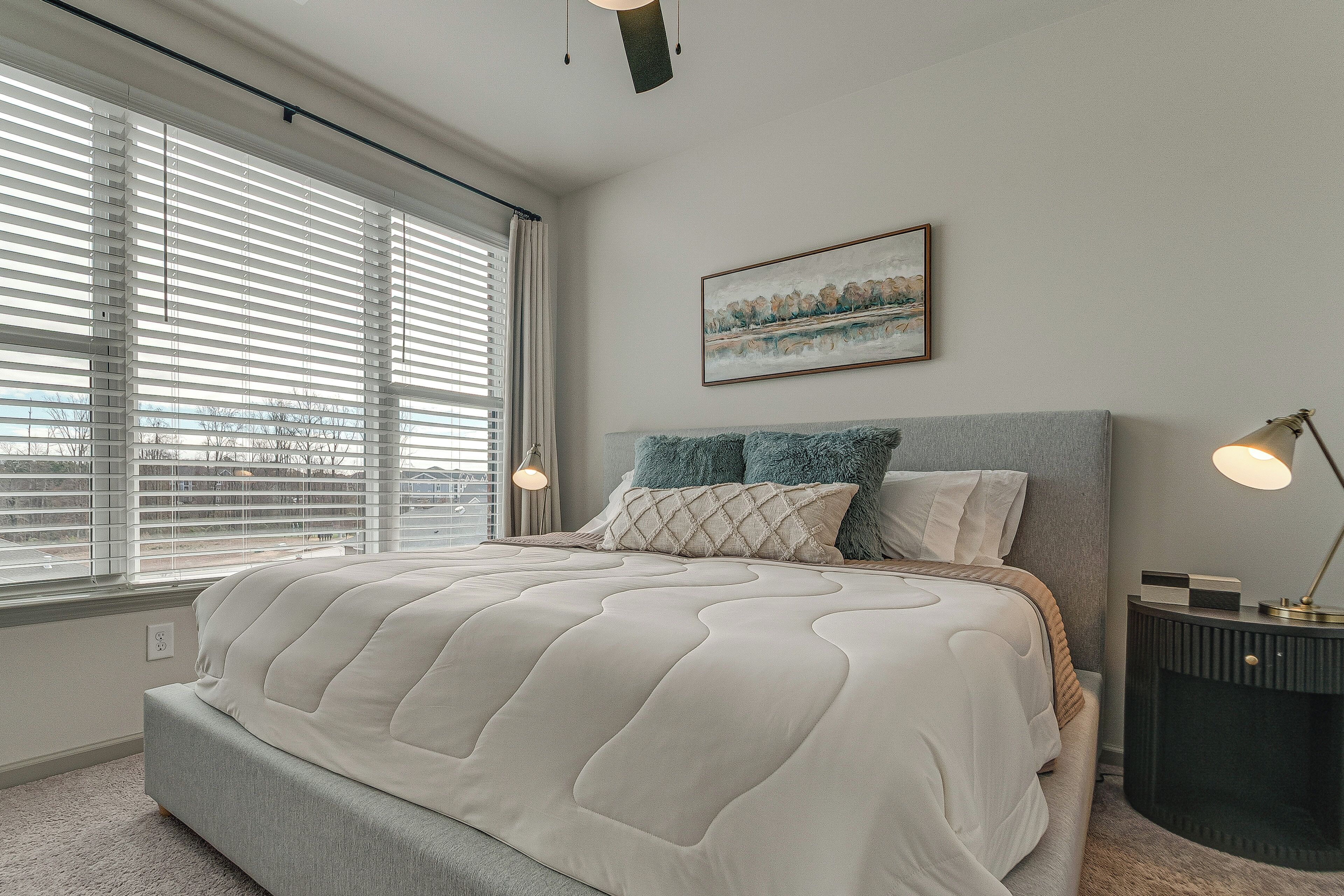 A bedroom with a large bed, a nightstand, a lamp, and a painting on the wall.