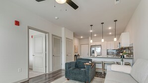 A modern living room with a grey armchair, a white sofa, and a kitchen area in the background.