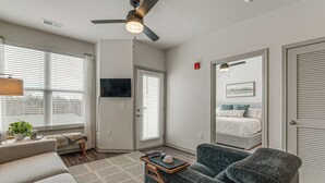 A modern living room with a sofa, a coffee table, a ceiling fan, and a large window with blinds.