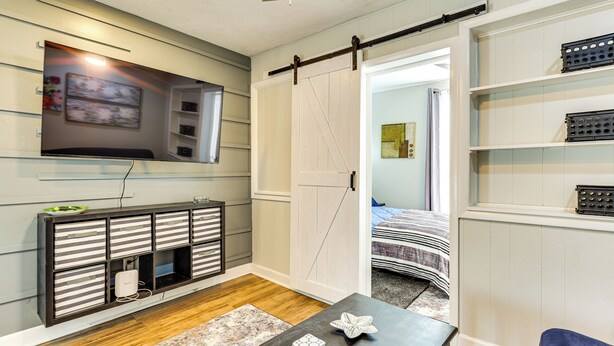 A modern living room with a flat-screen TV mounted on the wall, a sliding barn door closet, a wooden floor, and a blue chair.