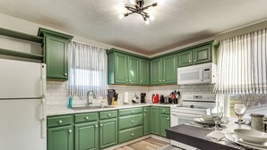 A kitchen with green cabinets, white appliances, and a wooden floor.