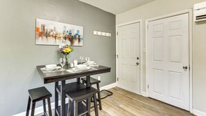 A dining area with a table set for four, a vase with flowers, and a cityscape painting on the wall.