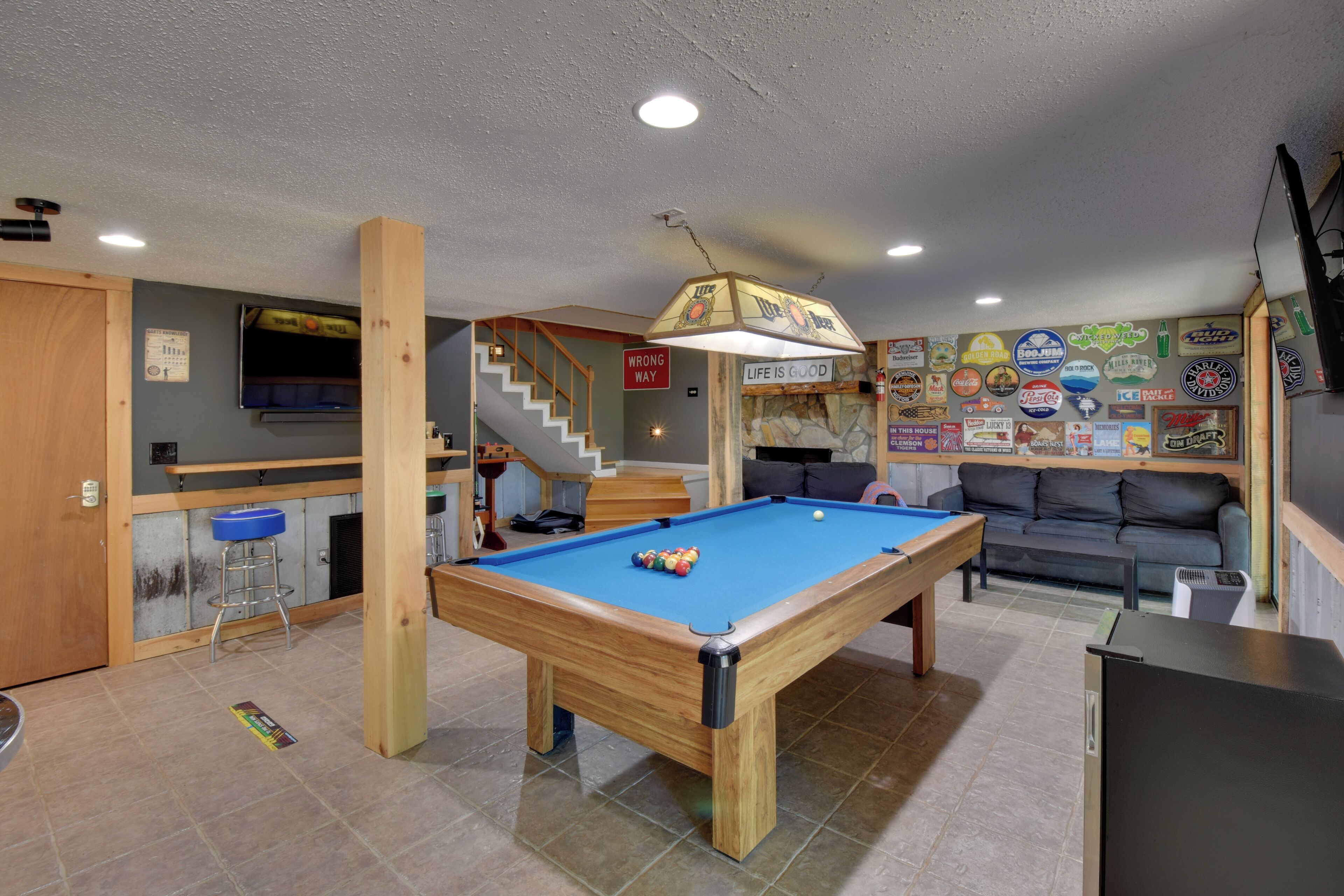Une table de billard dans une pièce avec un escalier, un canapé et un mur décoré de différents panneaux.