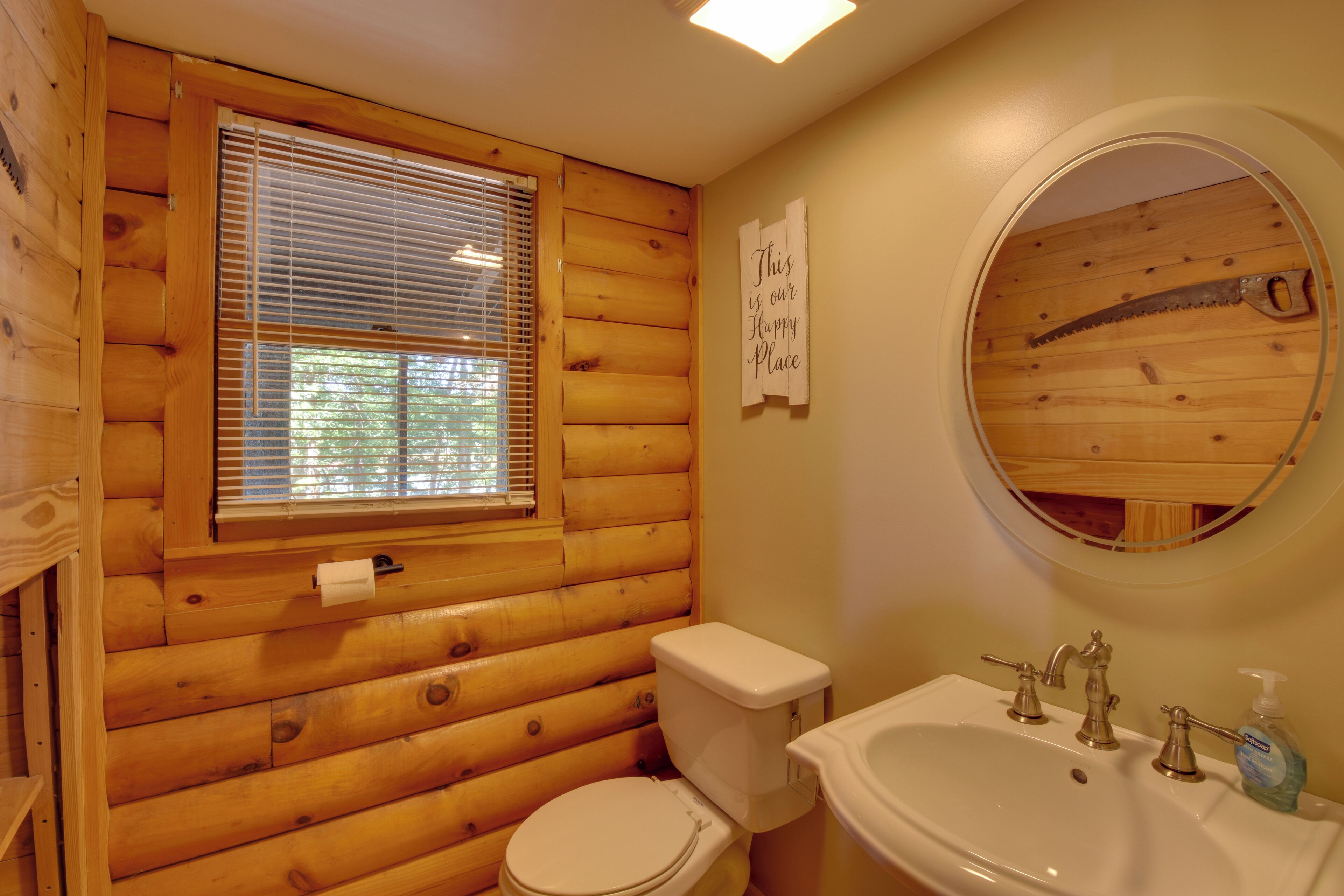 A wooden cabin bathroom with a toilet, sink, and window.