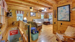 Interior de uma cabana de tronco com escada, sofá, um mapa na parede e um troféu de chifres de veado.