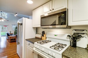 Una cocina con armarios blancos, un microondas de acero inoxidable, una estufa a gas y una encimera de granito.