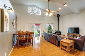 Un salón amplio con suelo de madera, ventilador de techo, chimenea, televisor y comedor con mobiliario de madera.