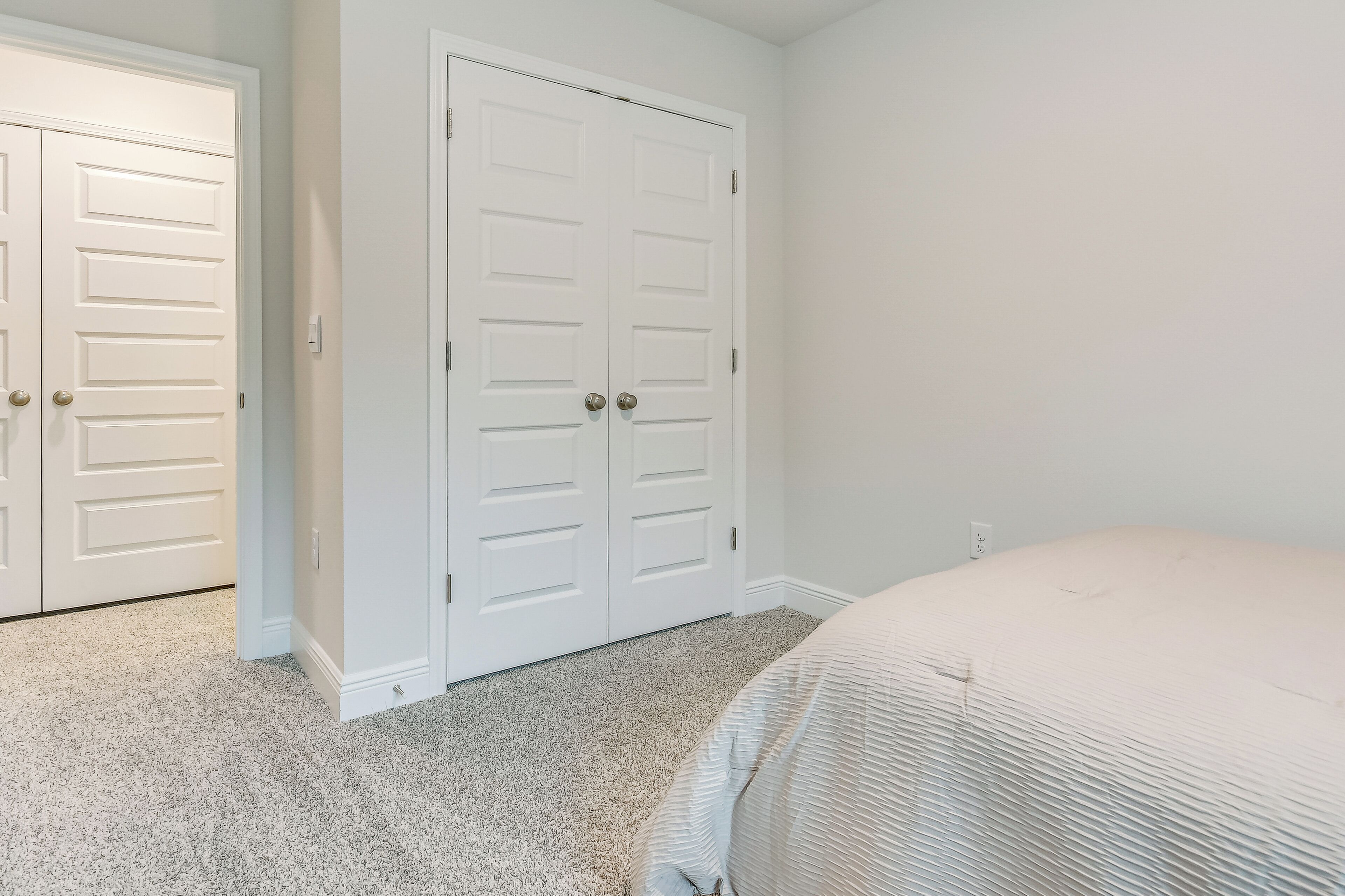 A bedroom with a bed, carpeted floor, and white double doors.