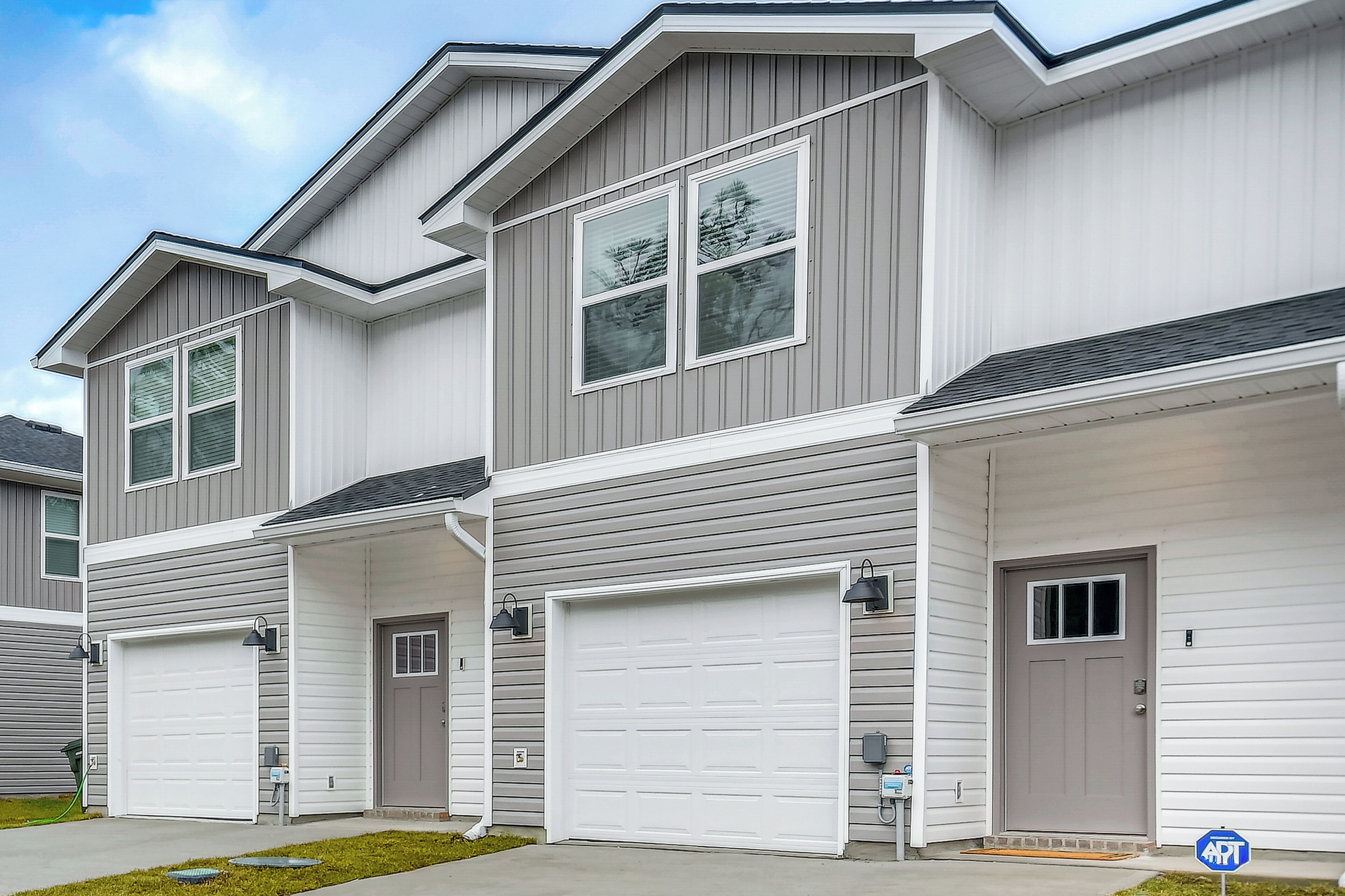 A row of townhouses with attached garages, a covered driveway, and a small front yard.