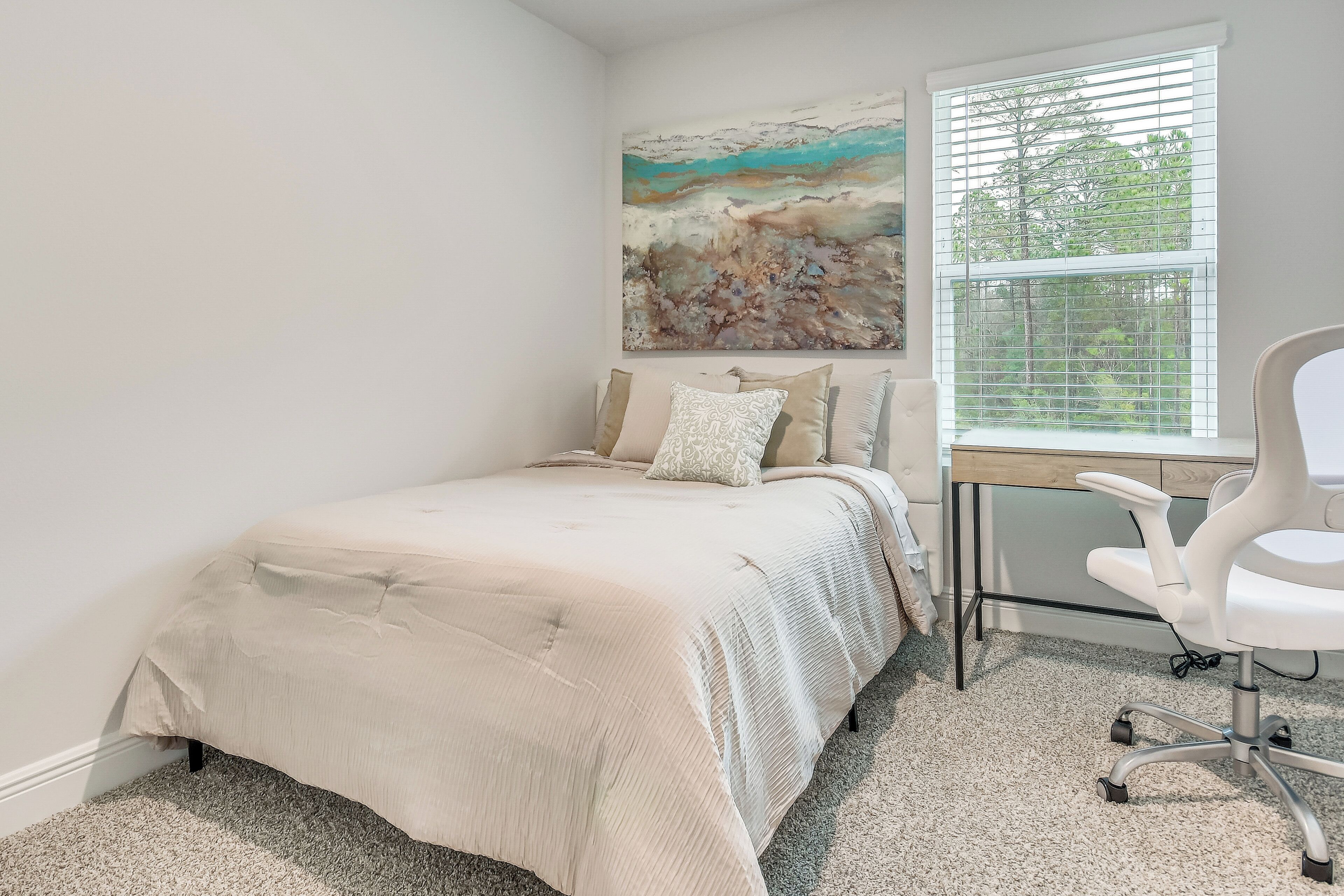 Une chambre à coucher avec un lit, un bureau avec une chaise, une fenêtre avec des stores et un tableau au mur.