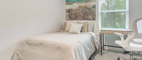Une chambre à coucher avec un lit, un bureau avec une chaise, une fenêtre avec des stores et un tableau au mur.