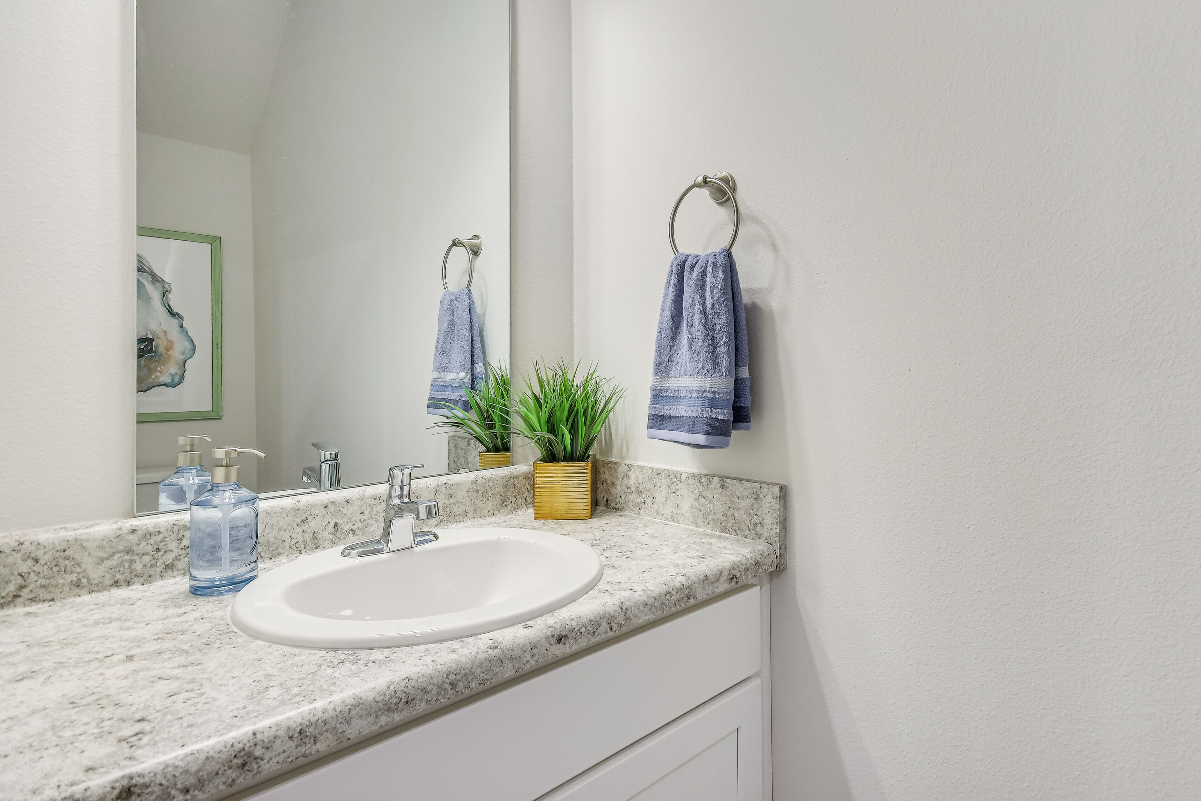 A bathroom with a white sink, a marble countertop, a mirror, and two towels hanging on a towel rack.