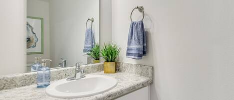 A bathroom with a white sink, a marble countertop, a mirror, and two towels hanging on a towel rack.
