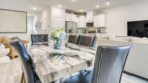 A modern kitchen with white cabinets, a large island, and a dining area with a marble table and leather chairs. - 8 Mi to Dtwn Pensacola: Modern Escape w/ Patio! (Pensacola)