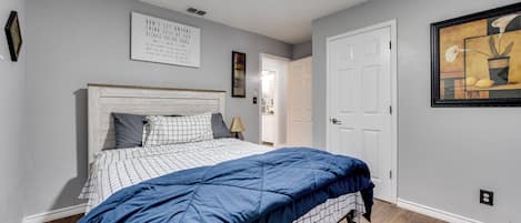 Une chambre à coucher avec un lit, un ventilateur de plafond, une porte et un mur orné d’un tableau encadré.