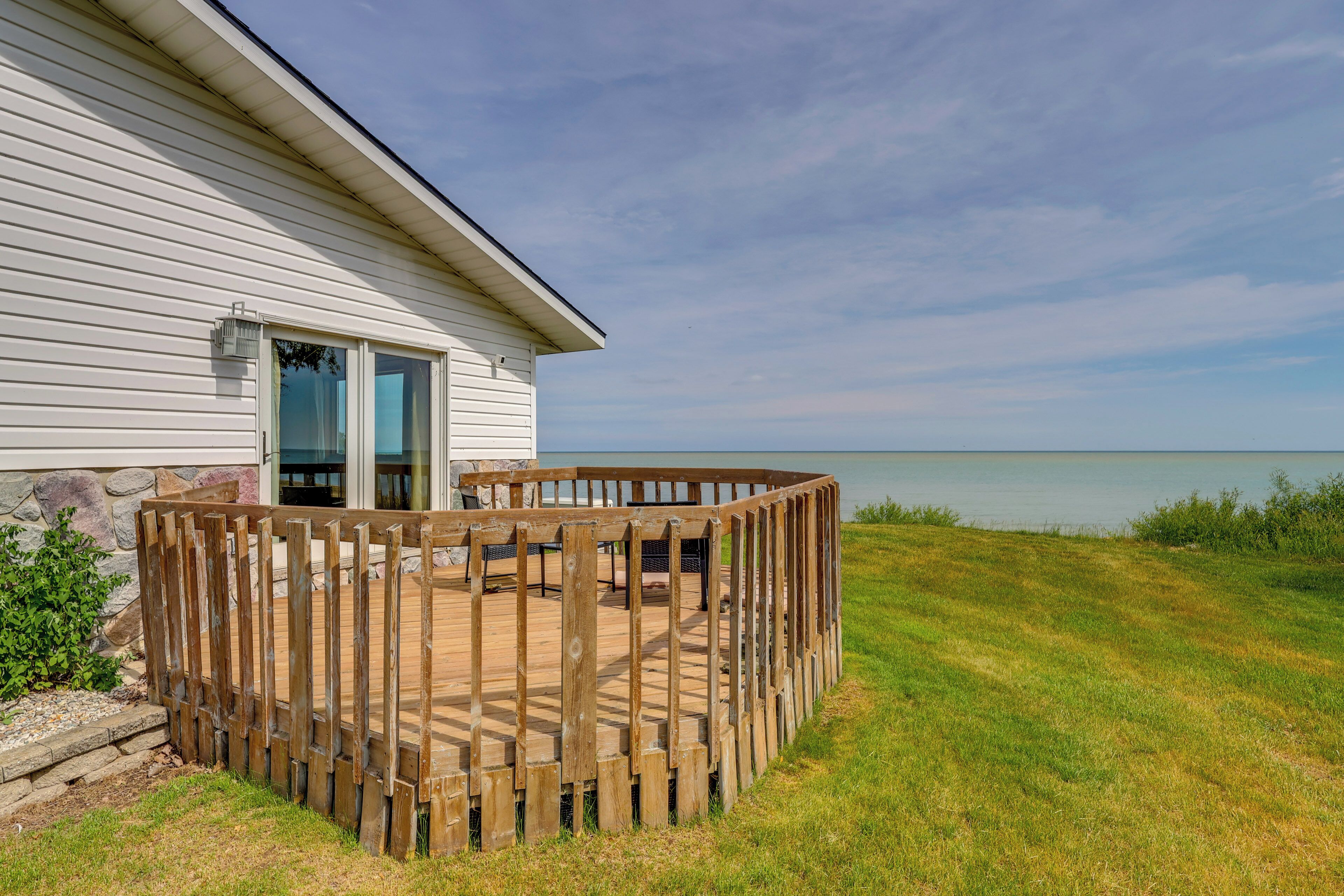 A wooden deck with a stone wall, a glass door, and a view of the water.