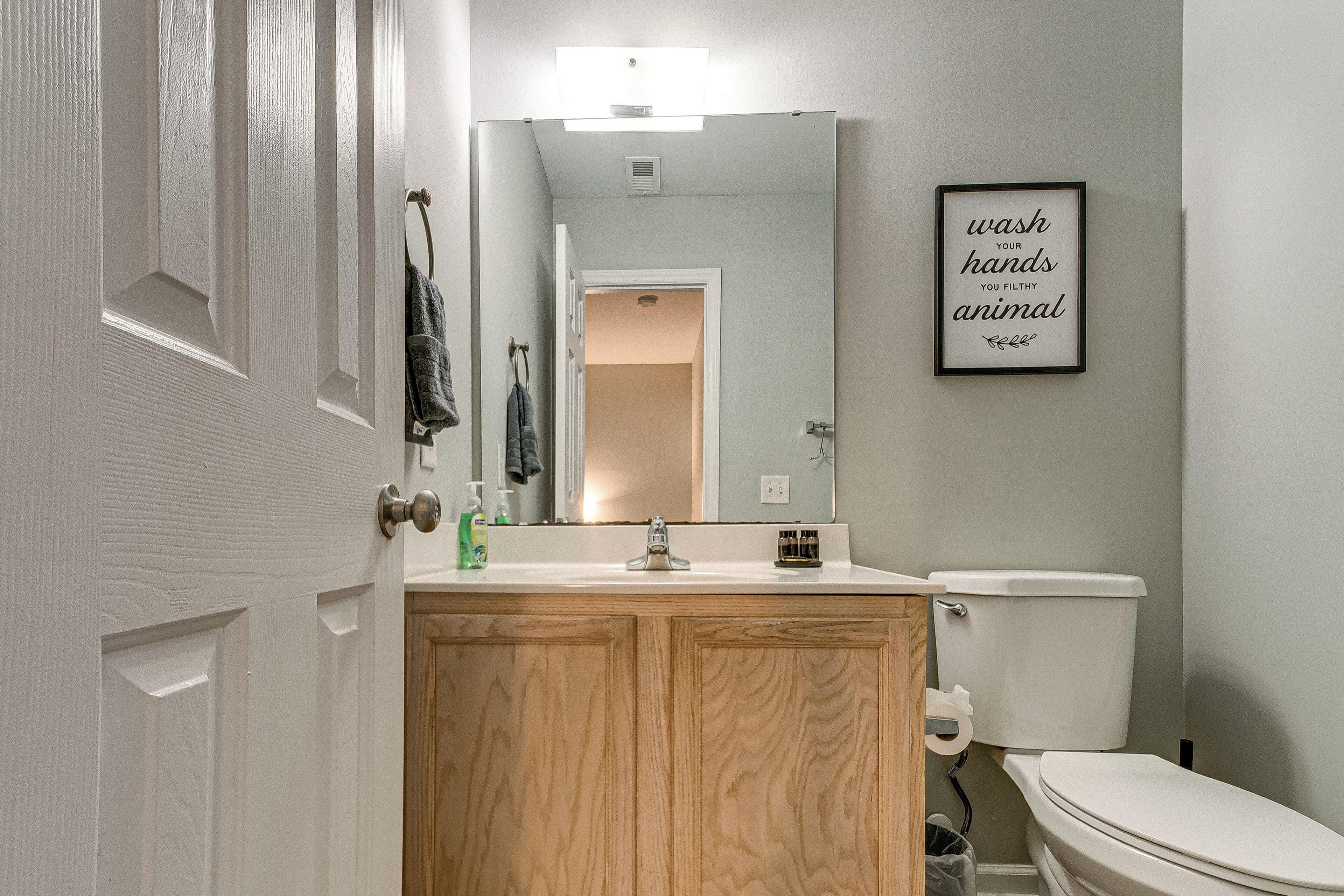 Un bagno con un mobile lavabo in legno, un water bianco e una citazione incorniciata al muro.