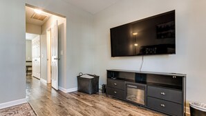 A modern living room with a flat-screen TV mounted on the wall, a dark wooden cabinet, and a patterned rug on the floor. - 2 Mi to Lenovo Center: Dog-friendly Getaway (Raleigh)