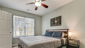 A bedroom with a bed, a ceiling fan, a window with blinds, a nightstand with a lamp, and a wall-mounted picture. - 2 Mi to Lenovo Center: Dog-friendly Getaway (Raleigh)