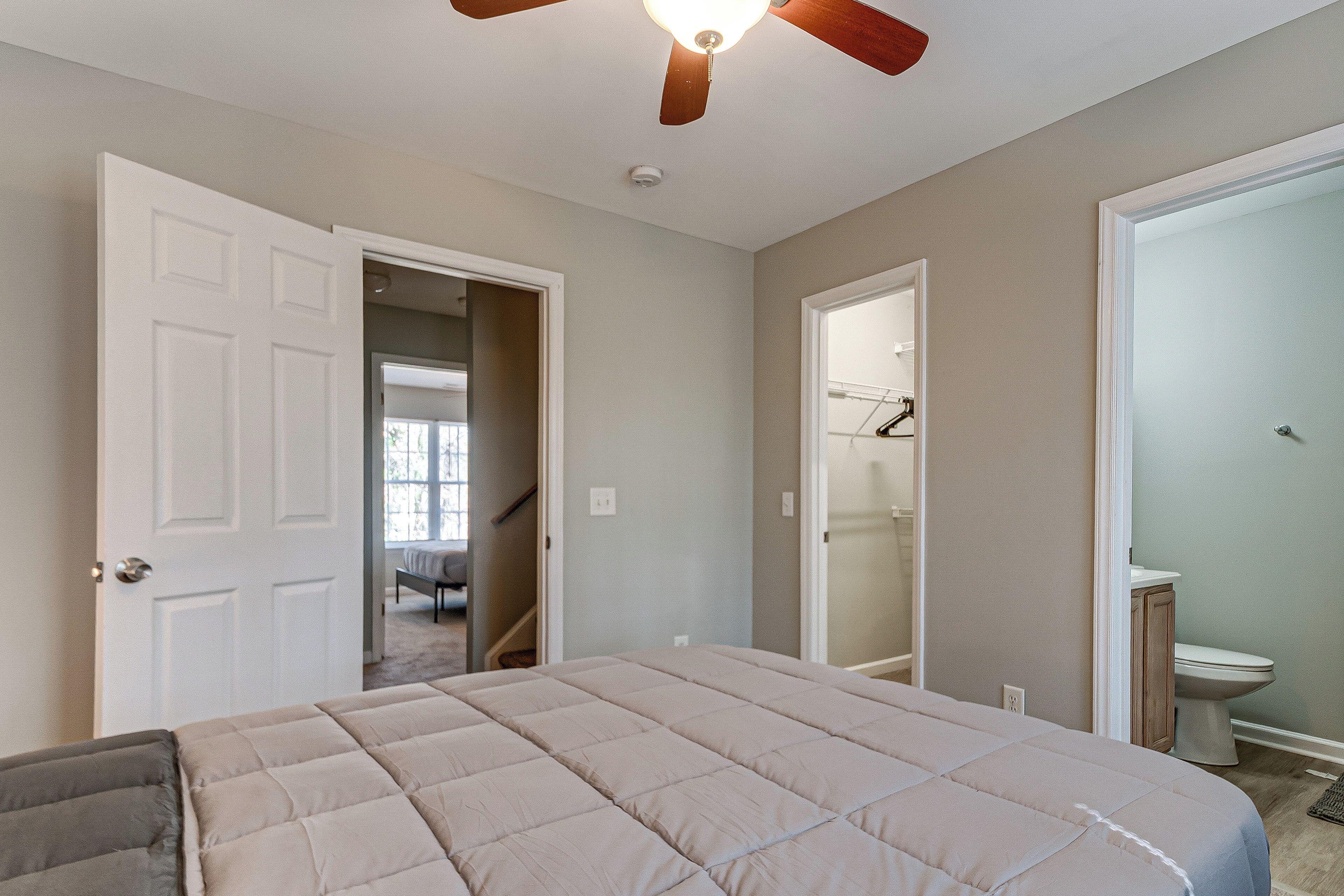 A bedroom with a bed, a ceiling fan, and a bathroom with a toilet and shower.