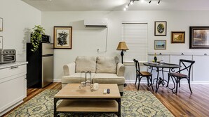 A living room with a sofa, coffee table, and dining area with chairs. There is a kitchen area with appliances and a refrigerator. - Golf, Shop & Unwind: Couple's Retreat in Naples! (Naples)