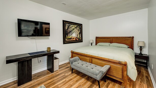 A bedroom with a wooden bed, a bench, a desk, a television, and a framed picture on the wall. - Golf, Shop & Unwind: Couple's Retreat in Naples! (Naples)