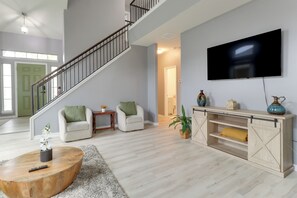 Ein geräumiges Wohnzimmer mit Treppe, einem Flachbildfernseher, einem Couchtisch aus Holz und einem Konsolentisch mit Dekorationselementen.