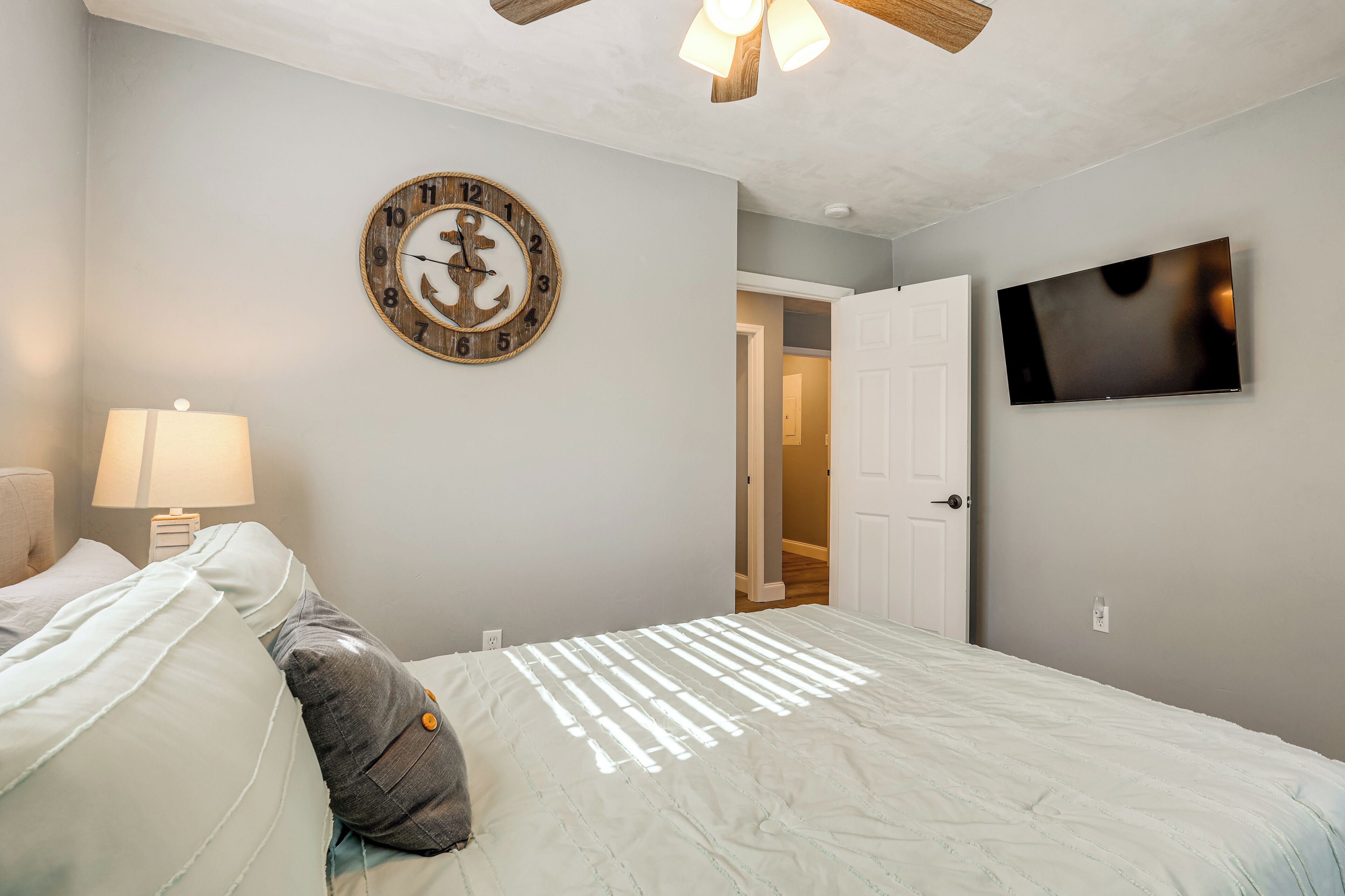 A bedroom with a bed, a wall clock, a TV, and a door leading to another room.